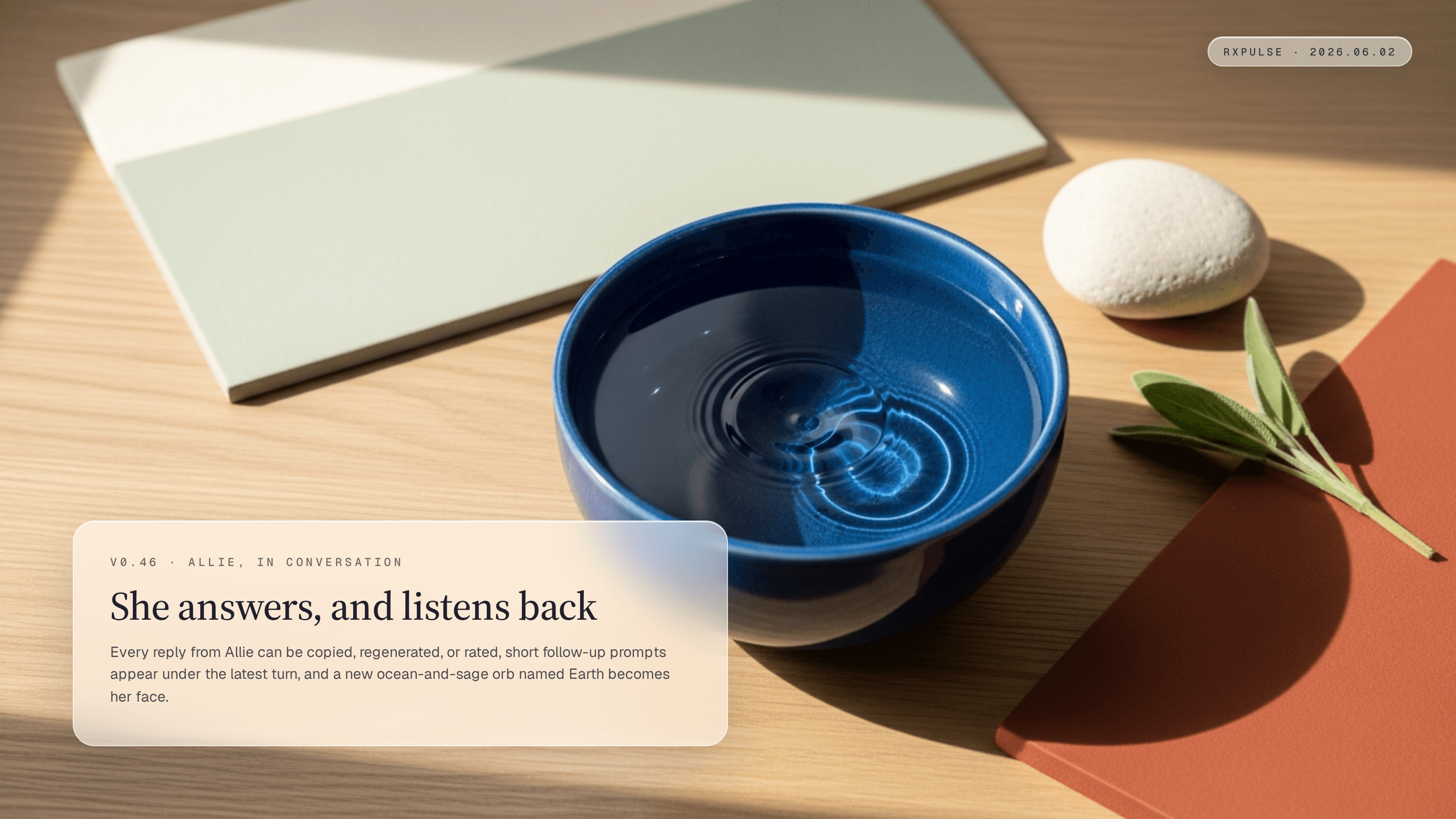 Editorial still life on pale oak in soft warm window light. A single round, deep ocean-blue glazed ceramic bowl holds still water that catches the light like a small planet seen from orbit, with two faint concentric ripples crossing its surface as if from sound. A smooth pale stone and a sprig of sage rest beside it. A glassmorphism caption card in the lower-left carries the eyebrow "v0.46 · ALLIE, IN CONVERSATION" with the headline "She answers, and listens back." and a short summary, and a monospace RxPulse brand pill sits in the top-right.